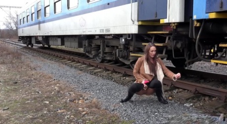Cynthia Vellons pulls down black tights for a quick piss near railway cars